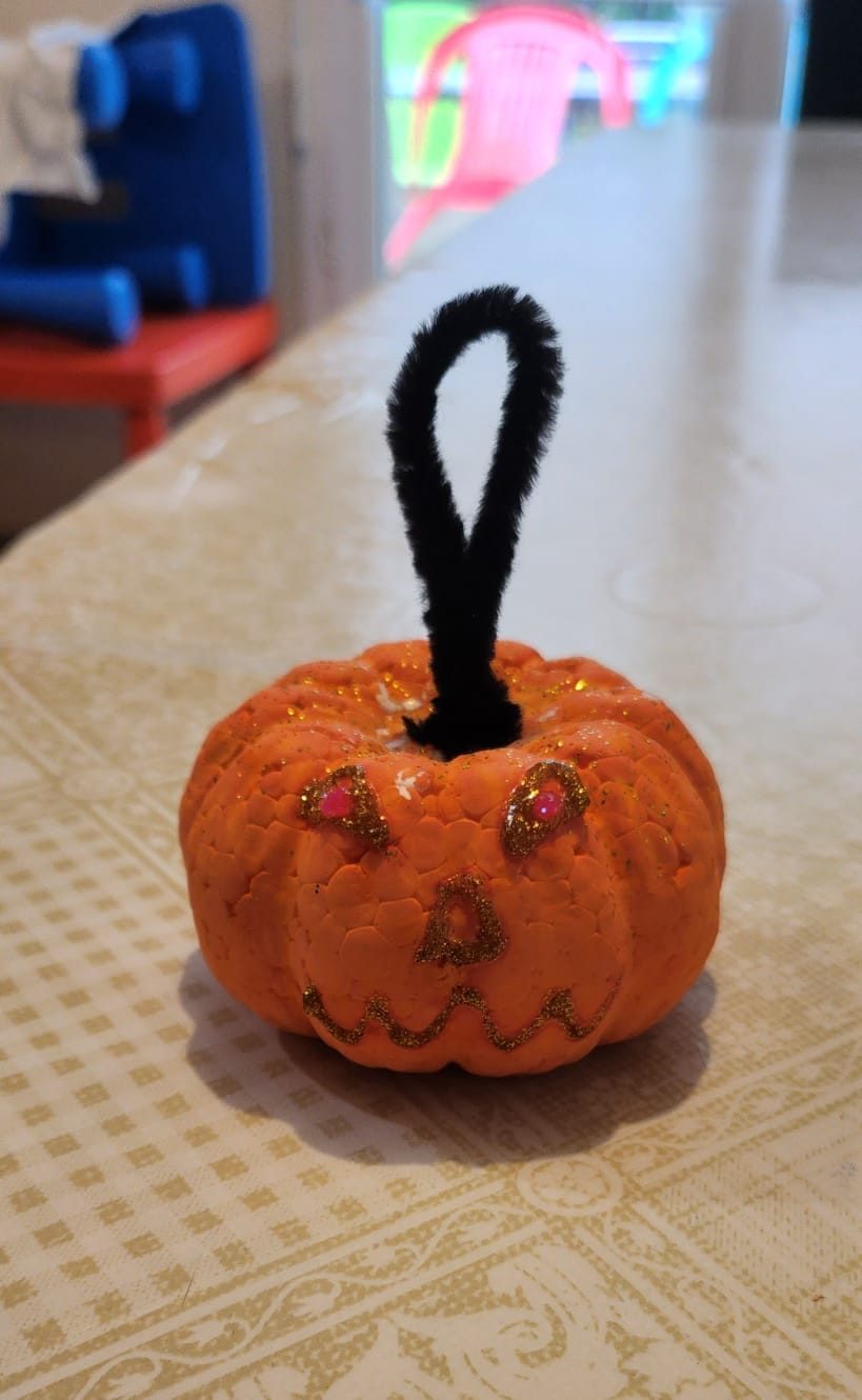 Petite citrouille d'Halloween en pâte à modeler orange, avec un visage souriant tracé en paillettes dorées et une tige e