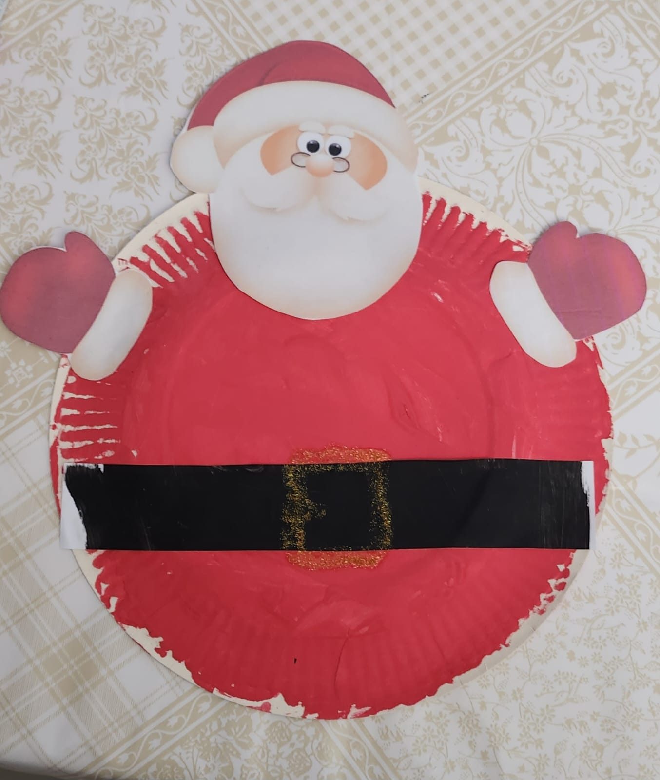 Père Noël bricolé sur une assiette en carton peinte en rouge, avec une ceinture noire et une boucle en paillettes dorées